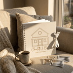 Personalised album with house illustration and 'Charlotte & Ben' text on a couch with a mug and photo frames.