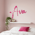 Pink 'Ava' wall decor above a bed with a pink pillow and plant.
