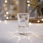 Clear shot glass with 'Ava' engraving on a textured surface with blurred lights in the background
