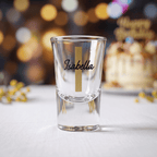 Clear shot glass with 'Isabella' engraving on a blurred festive background