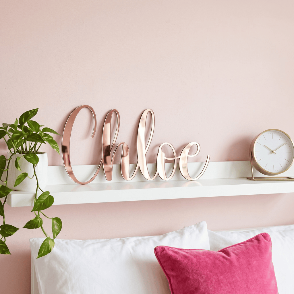 Decorative wall sign with 'Chloe' on a pink wall above a bed with pillows.