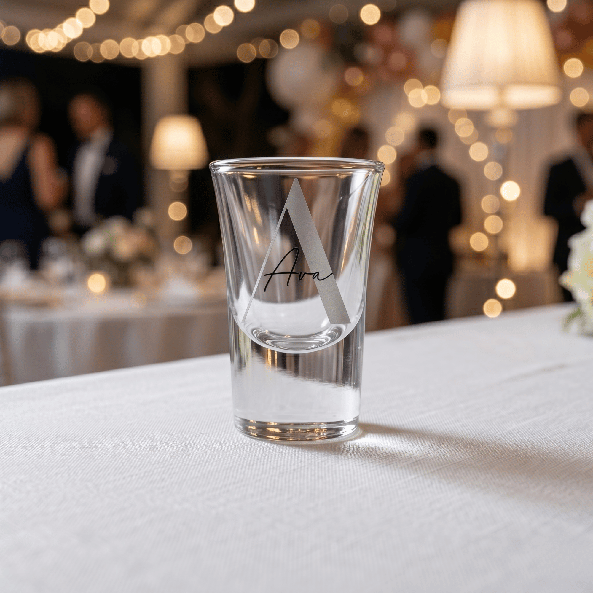 Clear shot glass with 'Avra' branding on a white tablecloth with blurred event background