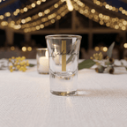 Clear shot glass with 'Isabella' engraving on a table with blurred lights in the background