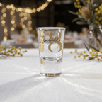 Clear glass with '18 Isabella' text on a white tablecloth with decorative elements