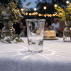 Clear glass with engraved text on a table with blurred background of people and lights