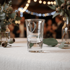 Clear glass shot glass with engraved text on a table with decorative elements