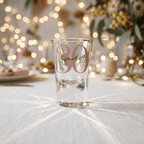 Clear shot glass with 'Scarlett' and '30' on a table with festive lights and decorations.