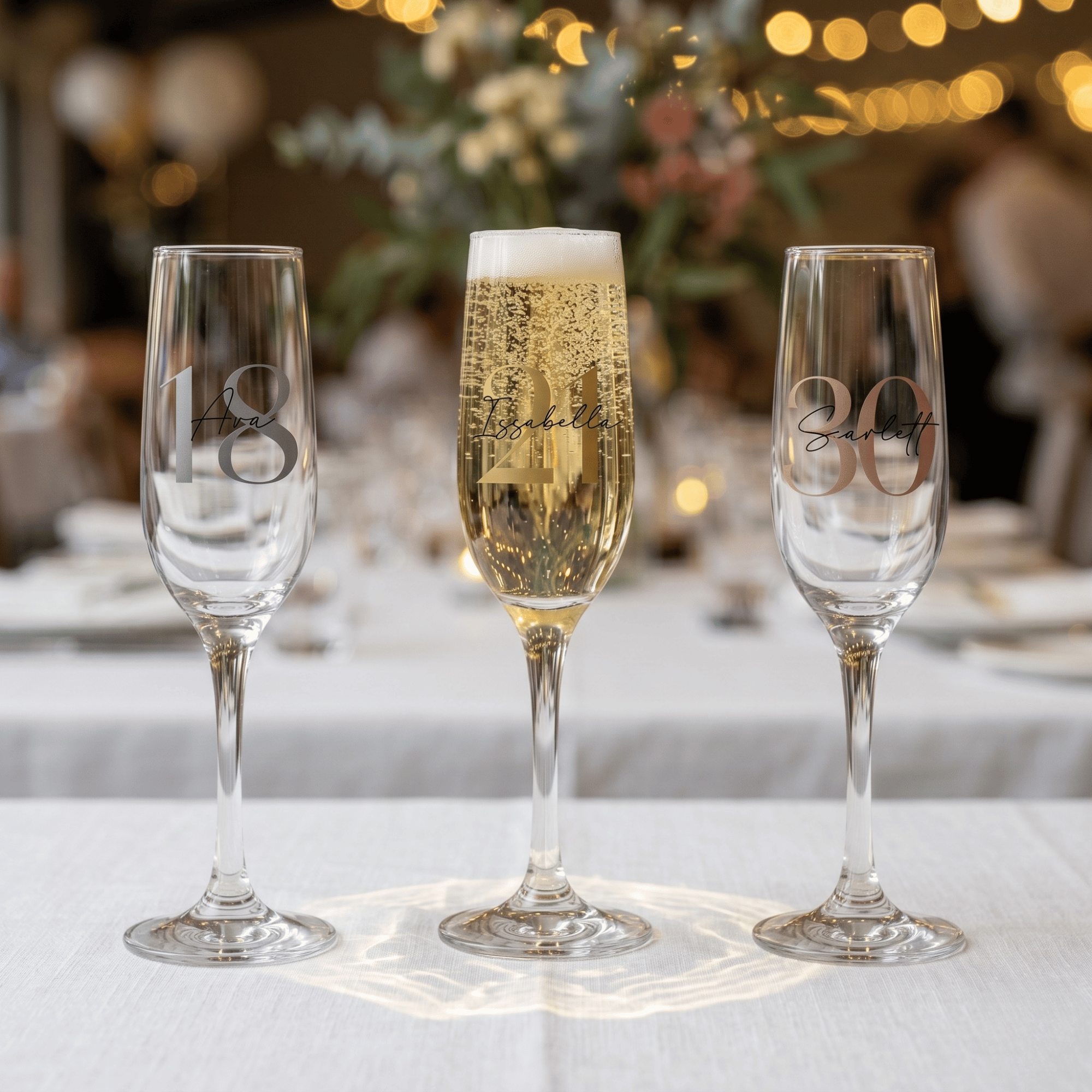 Three champagne flutes with engraved numbers on a table with a blurred festive background.