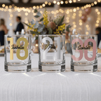 Three glass tumblers with personalized numbers and names on a blurred festive background