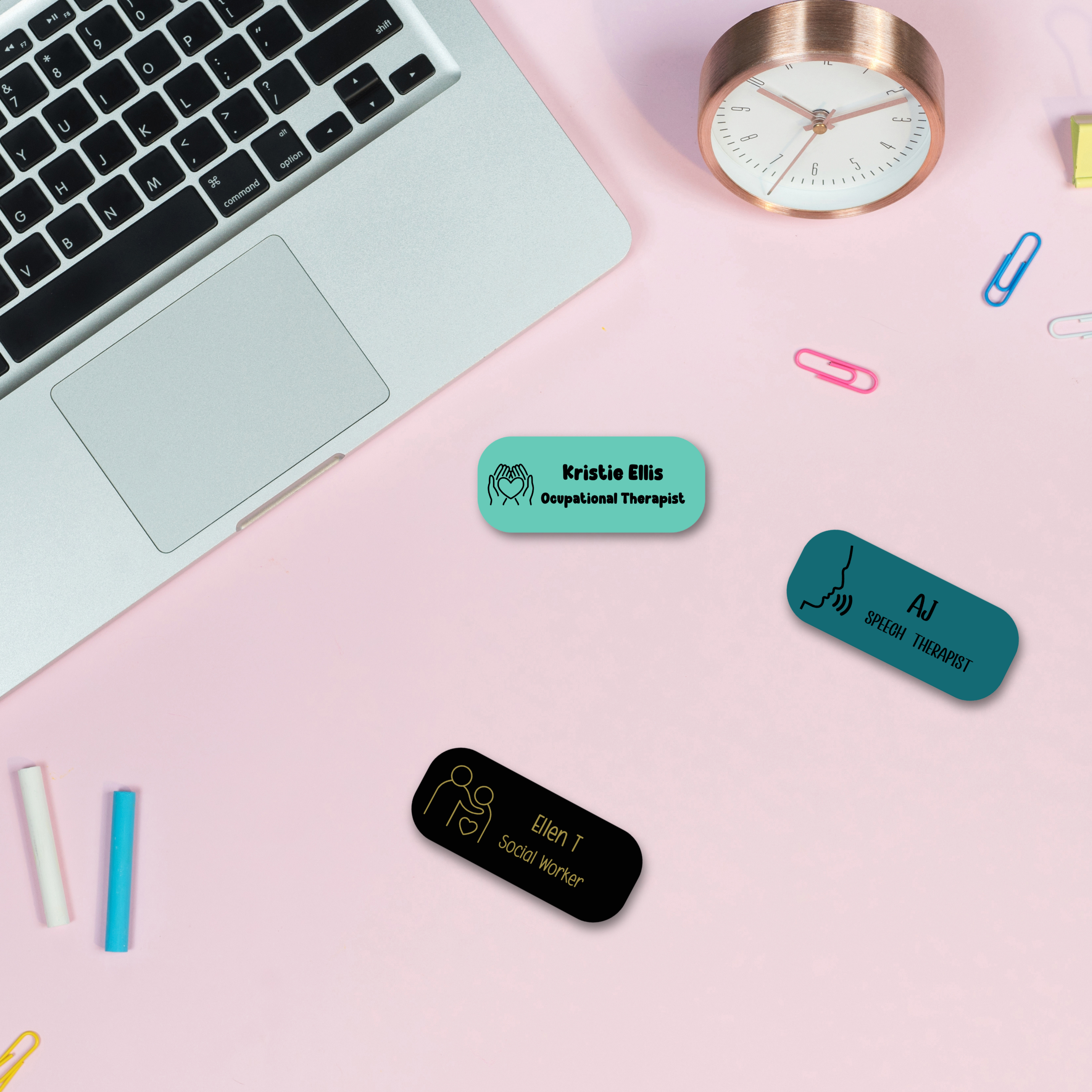 Personalised medical name badges for healthcare professionals including occupational therapist, speech therapist, and social worker. Flat lay on pink background with laptop.