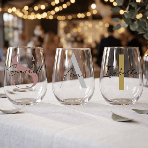 Three personalized stemless wine glasses on a table with blurred background