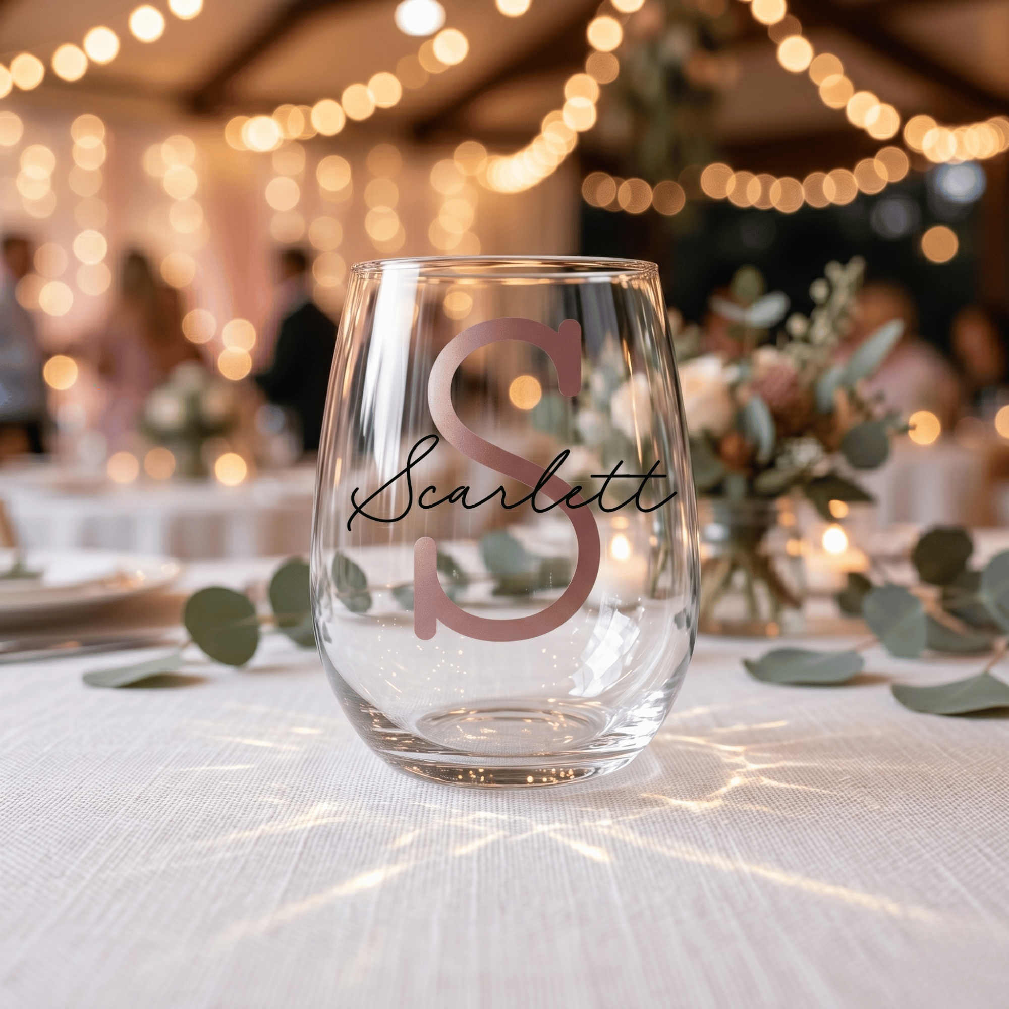 Clear wine glass with 'Scarlett' and monogram on a blurred wedding reception background