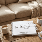 Personalised Album titled 'The Story of Us' on a wooden table with a cup and cards, against a beige sofa background.