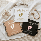 Three baby-themed Albums for a baby shower on a soft fabric background with baby shoes and a teething ring.