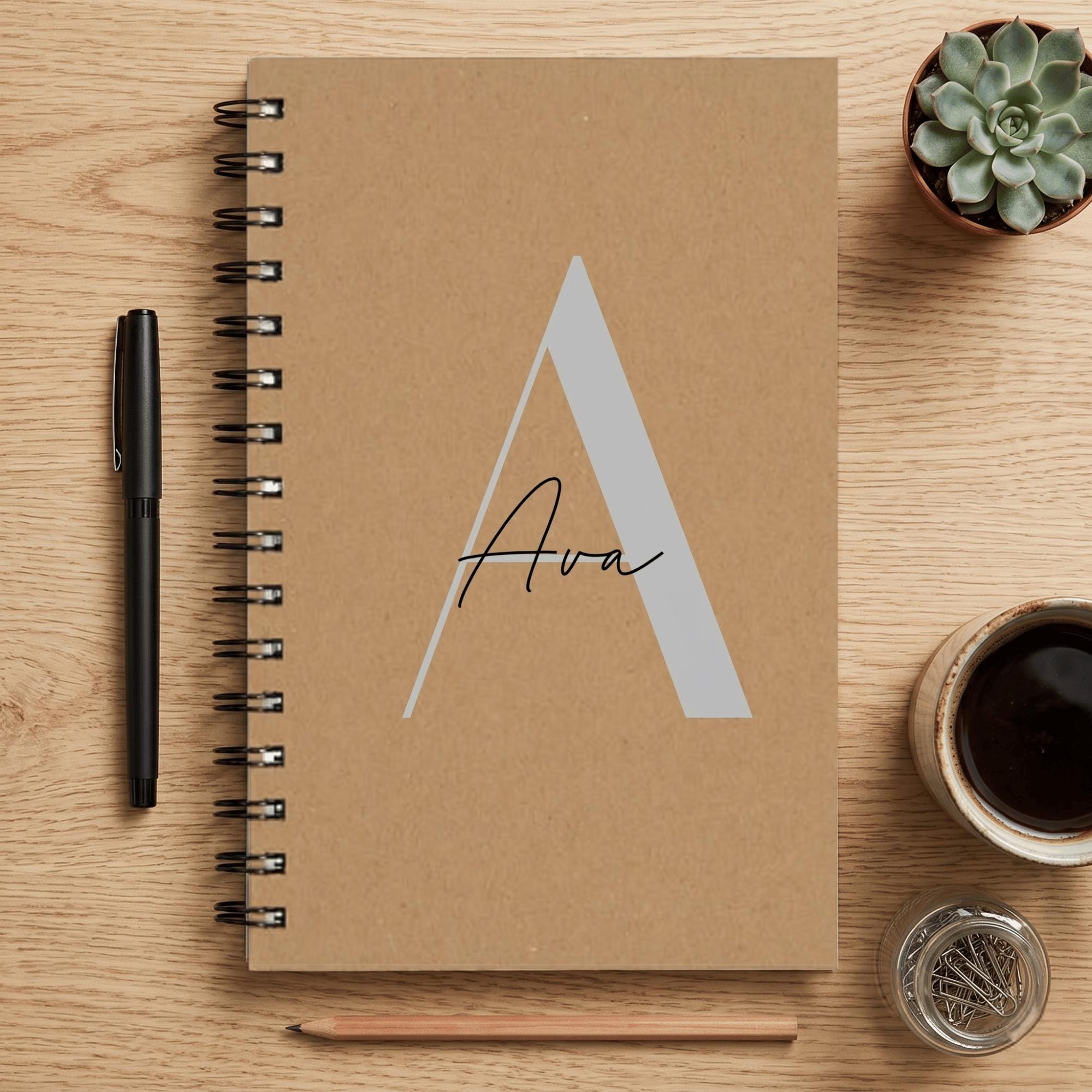 Brown notebook with 'Ava' on a wooden surface with stationery items.