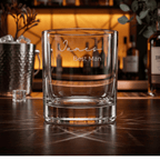 Clear glass with engraved text 'James Best Man' on a wooden surface with blurred bar background