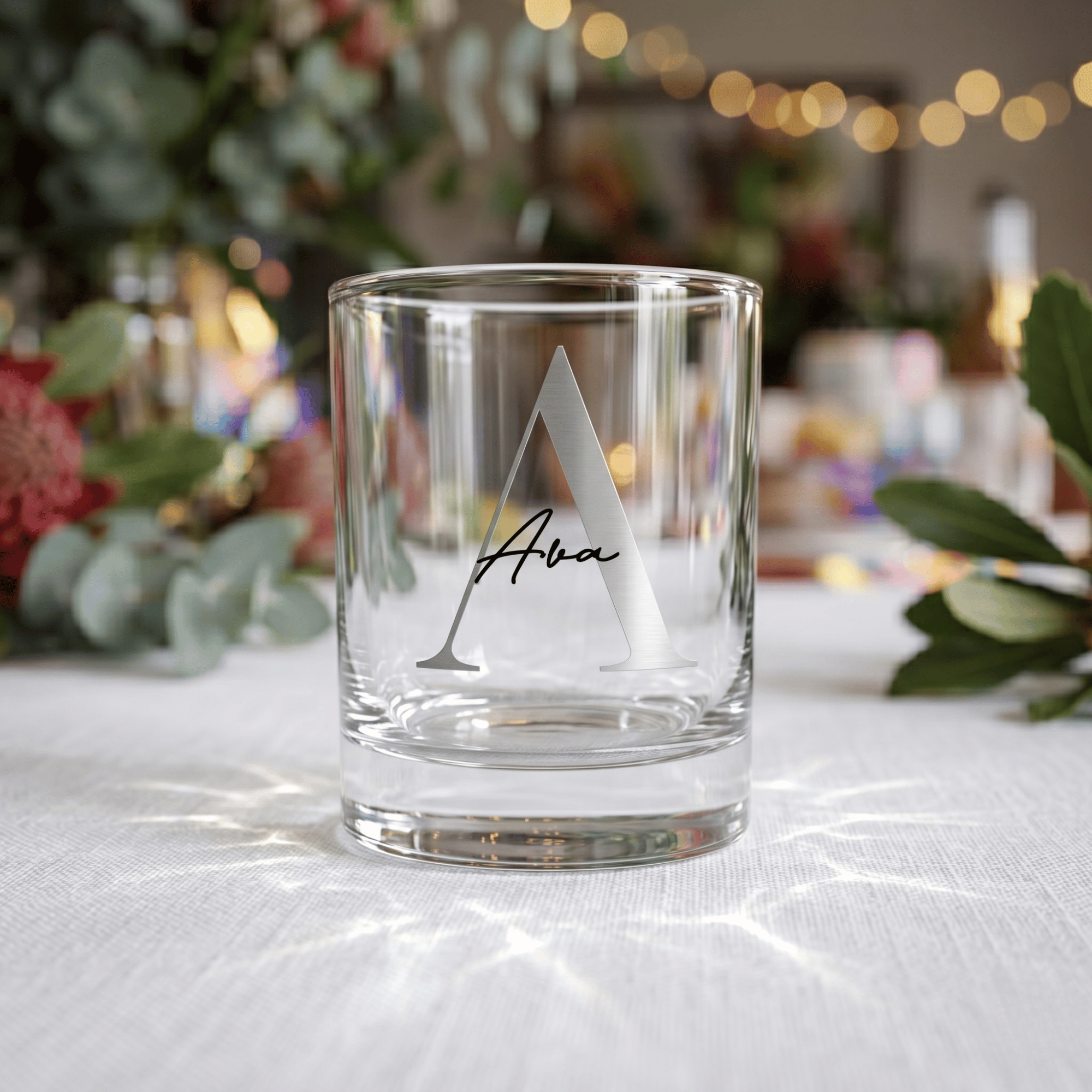Clear glass with engraved letter 'A' and name on a white surface with decorative background