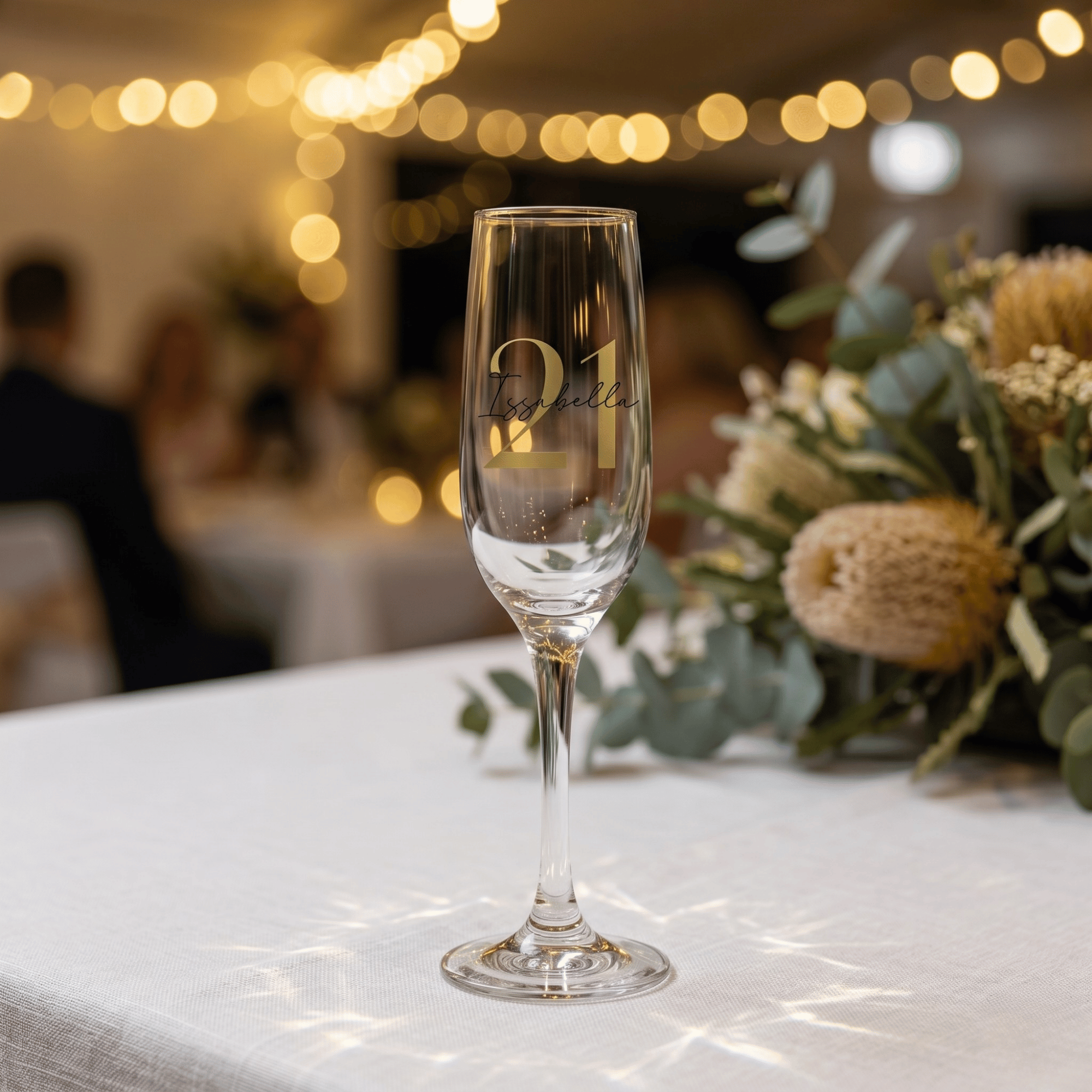 Champagne flute with '21' and 'Issabella' text on a table with blurred background
