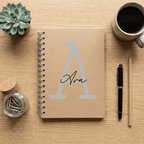 Notebook with 'Ava' on a wooden surface with a plant, mug, and pen.