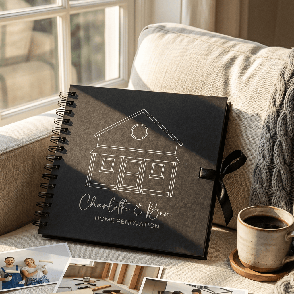 Black album with house illustration and text on a couch with a cup of coffee and photos.