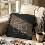 Black album with house illustration and text on a couch with a cup of coffee and photos.