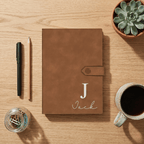 Brown notebook with 'Jack' on a wooden surface with a pen, coffee, and plant.