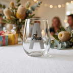 Clear glass with 'Ava' engraving on a table with decorative elements and people in the background