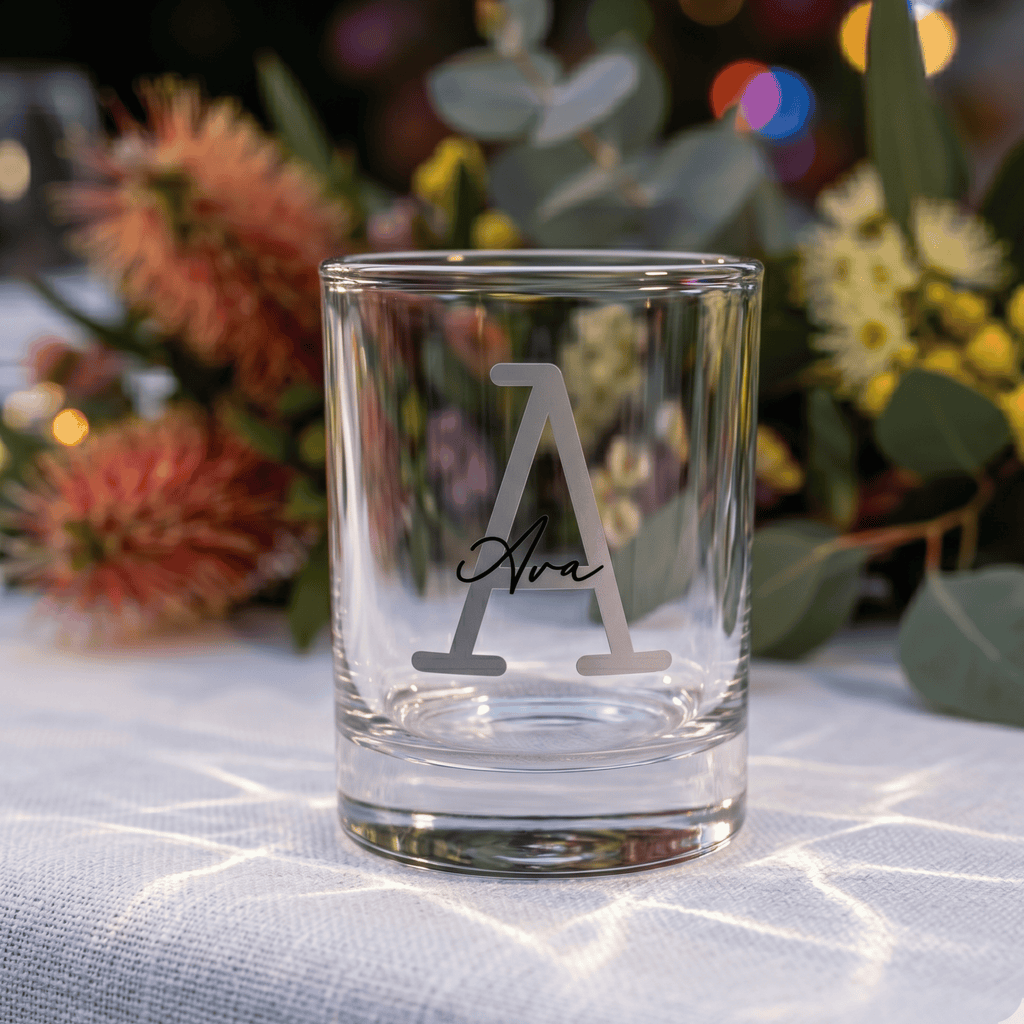 Clear glass with engraved design on a tablecloth with flowers in the background