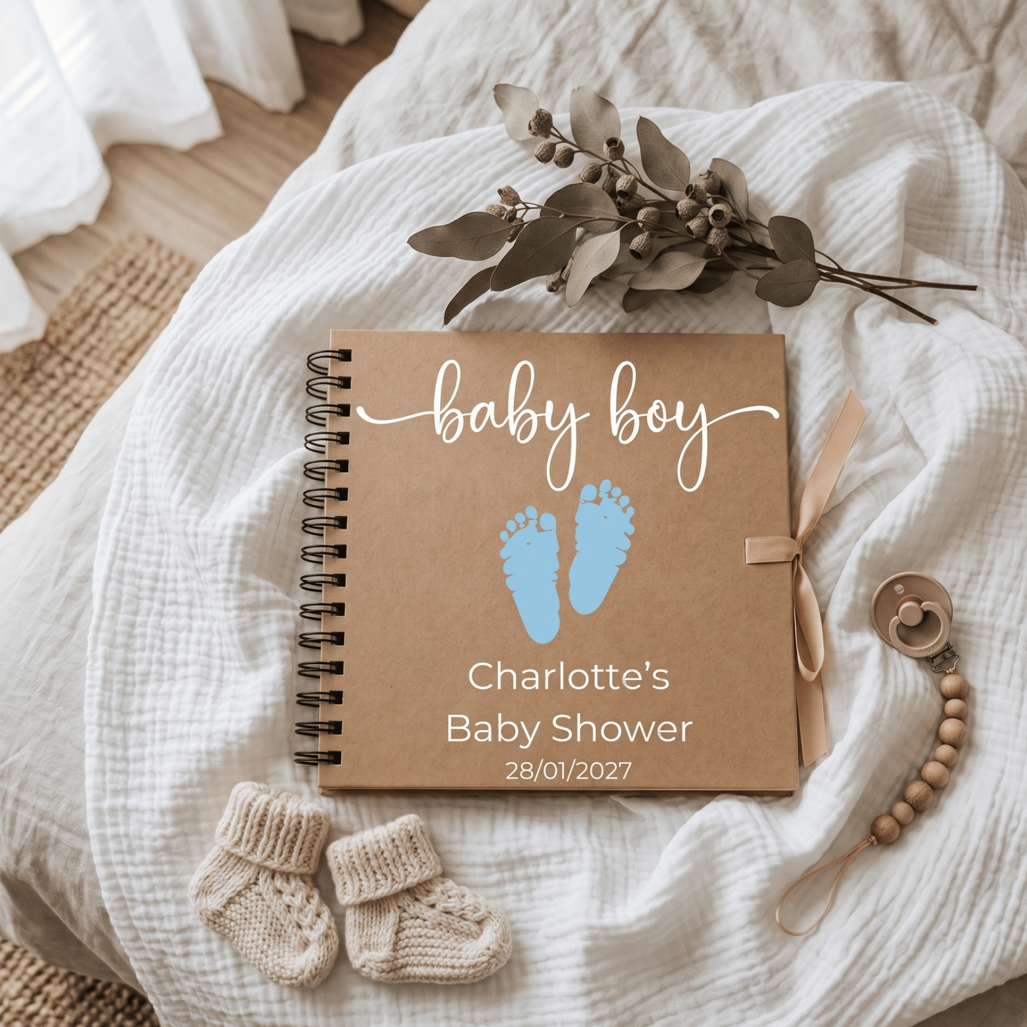 Album with 'baby boy' text and footprints, surrounded by baby items on a soft fabric background
