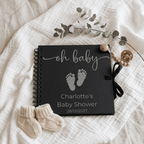 Black baby album with 'oh baby' text and baby feet design on a textured surface with baby booties and a branch.