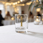 Clear glass with gold letter 'I' and name 'Isabella' on a white tablecloth with blurred lights in the background
