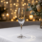 Champagne flute with 'L' monogram on a white surface with blurred lights and flowers in the background