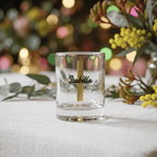 Clear glass with 'Isabella' engraving on a table with decorative plants and blurred lights in the background