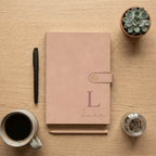 Pink notebook with 'Luna' on a wooden surface with a pen, mug, and plant.