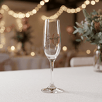 Champagne flute with 'Scarlett' engraved on a table with decorative lights and plants in the background