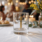Clear glass with a candle labeled 'Isabella' on a table with blurred background