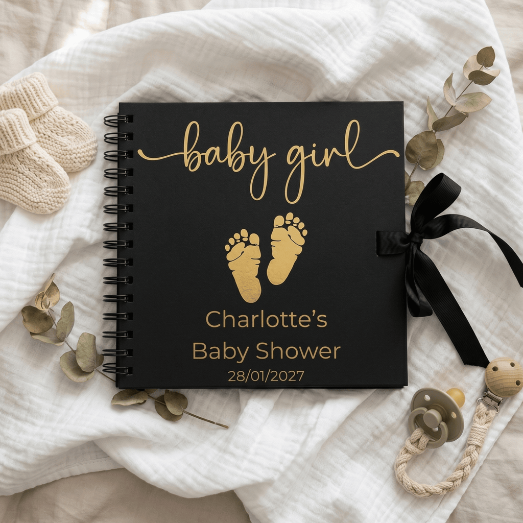 Black Album with 'baby girl' and footprints for a baby shower on a soft fabric background.