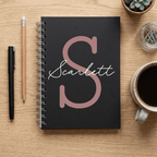 Black notebook with 'Scarlett' on a wooden surface with stationery items.