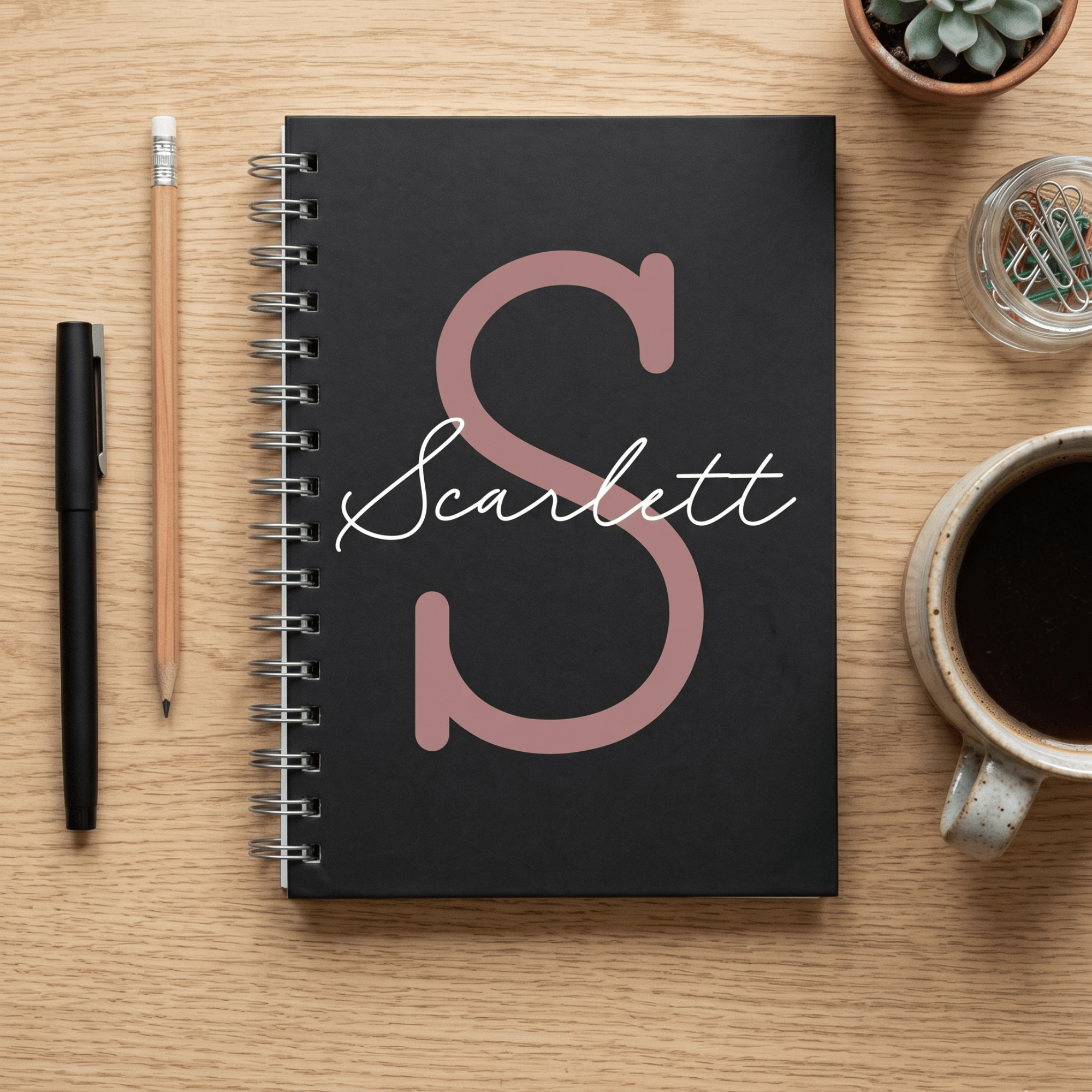Black notebook with 'Scarlett' on a wooden surface with stationery items.