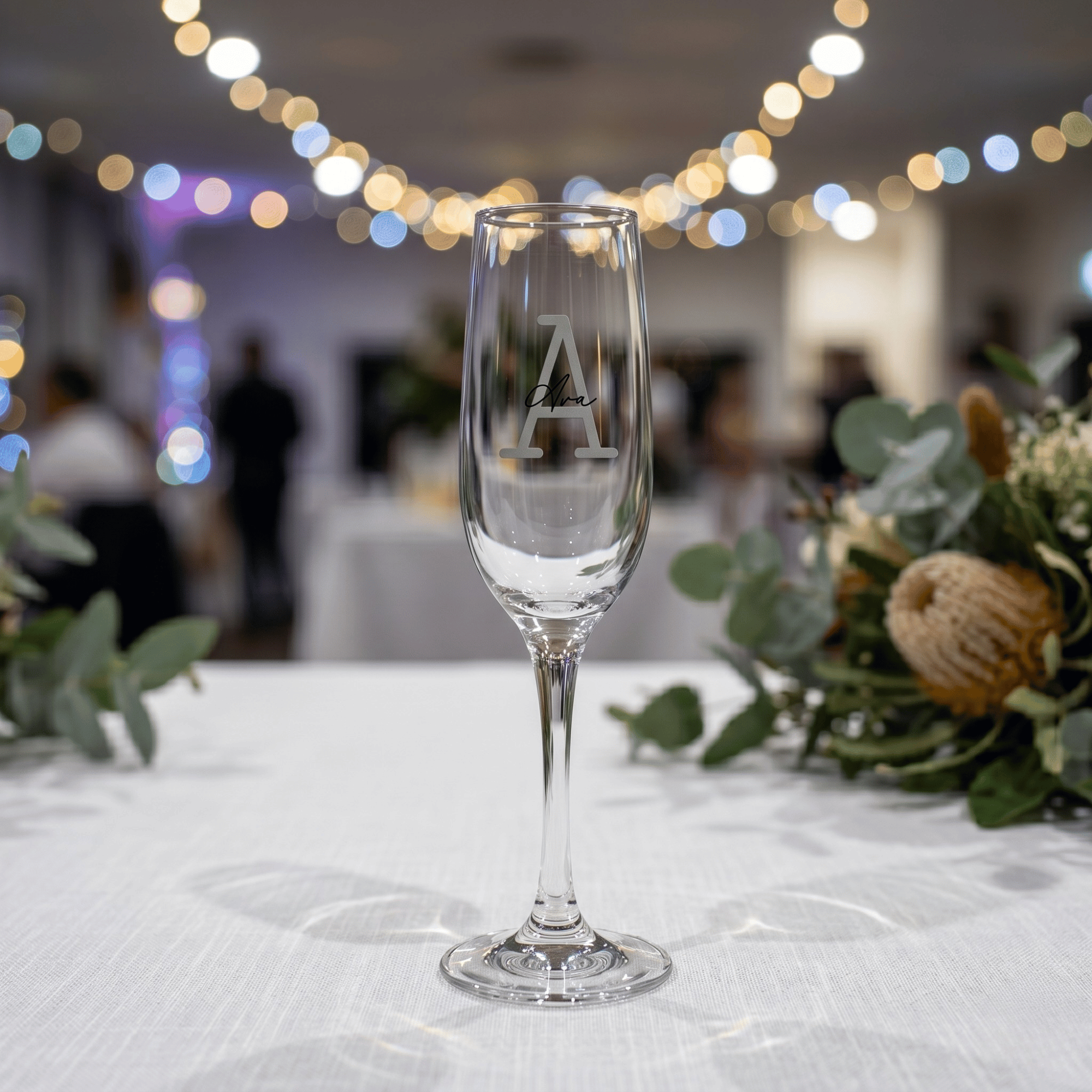 Clear glass with a monogram 'A' on a table with decorative elements and blurred lights in the background