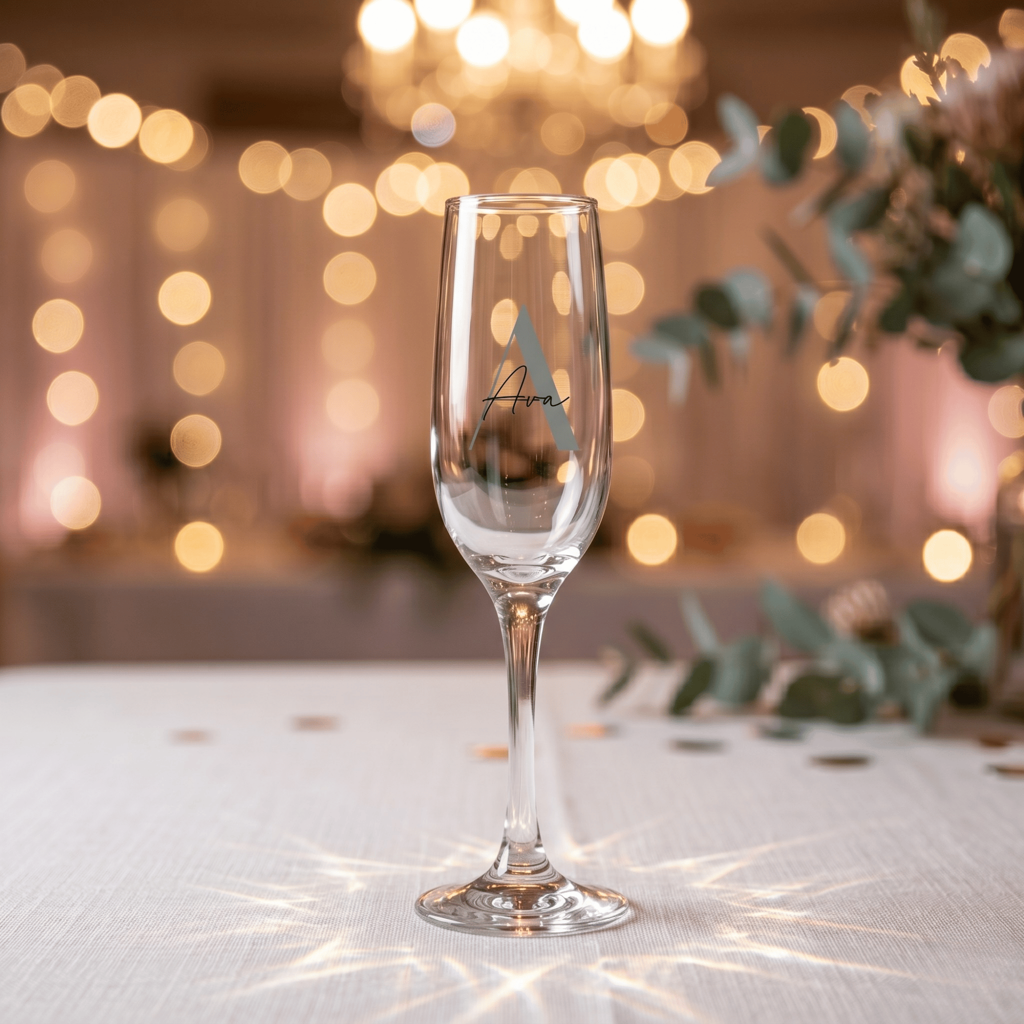 Clear champagne flute with 'Ava' engraving on a blurred festive background