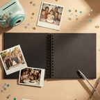 Black spiral-bound Album with photos of a birthday celebration on a wooden surface.