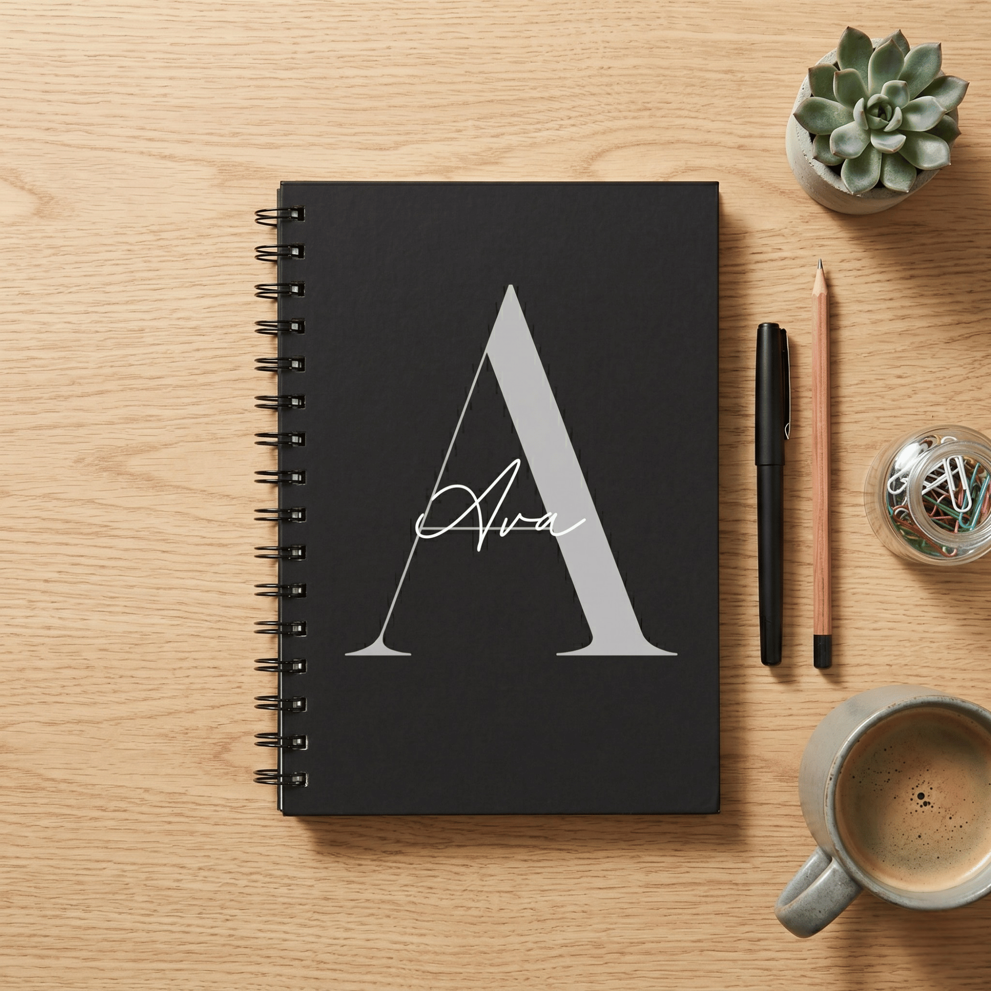 Black notebook with 'Ava' on a wooden surface with stationery items
