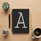 Black notebook with a white letter 'A' design on a wooden table with stationery items.