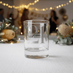 Clear glass with '21 Ava' engraving on a table with decorative items and string lights in the background