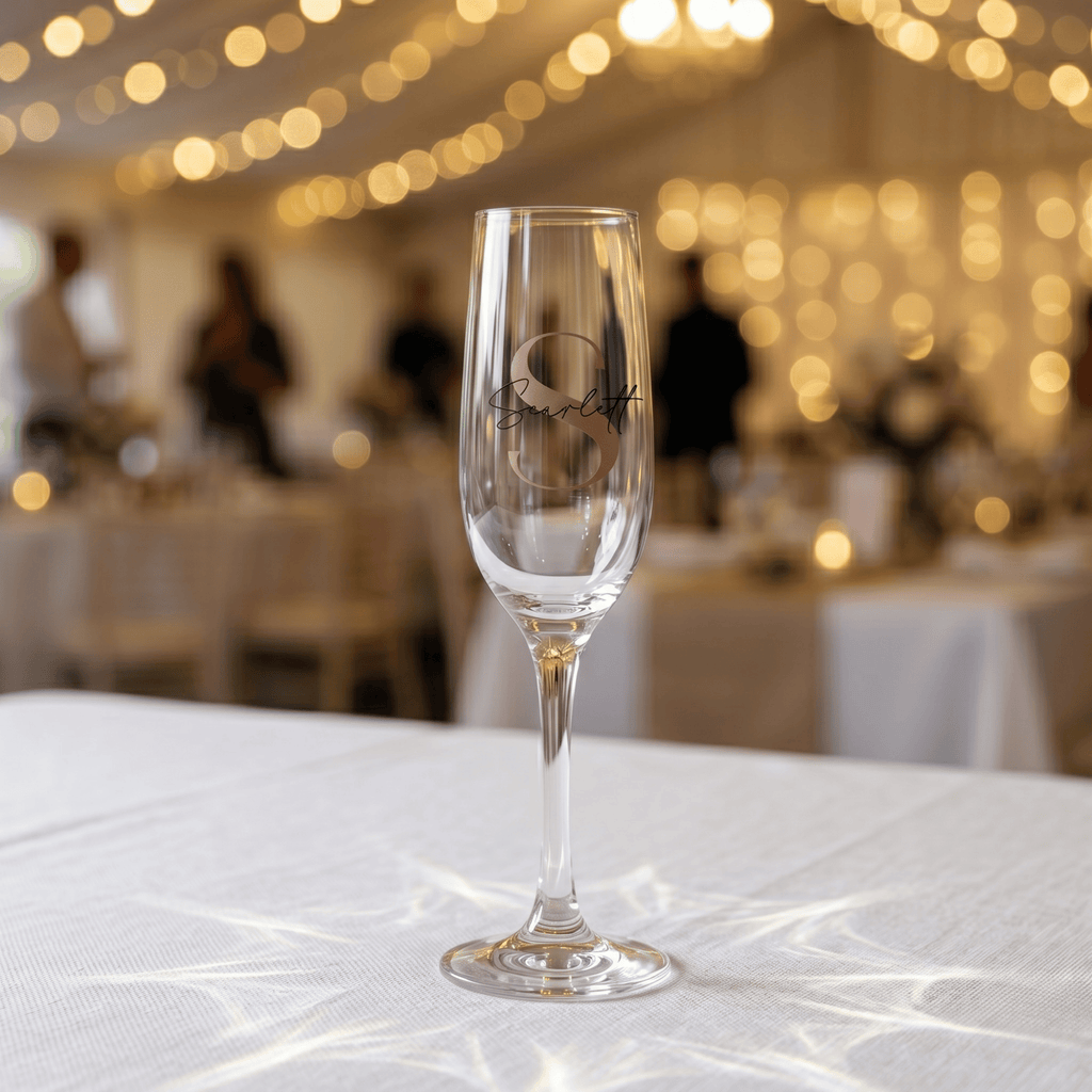 Champagne flute with 'S' monogram on a tablecloth in a festive indoor setting.