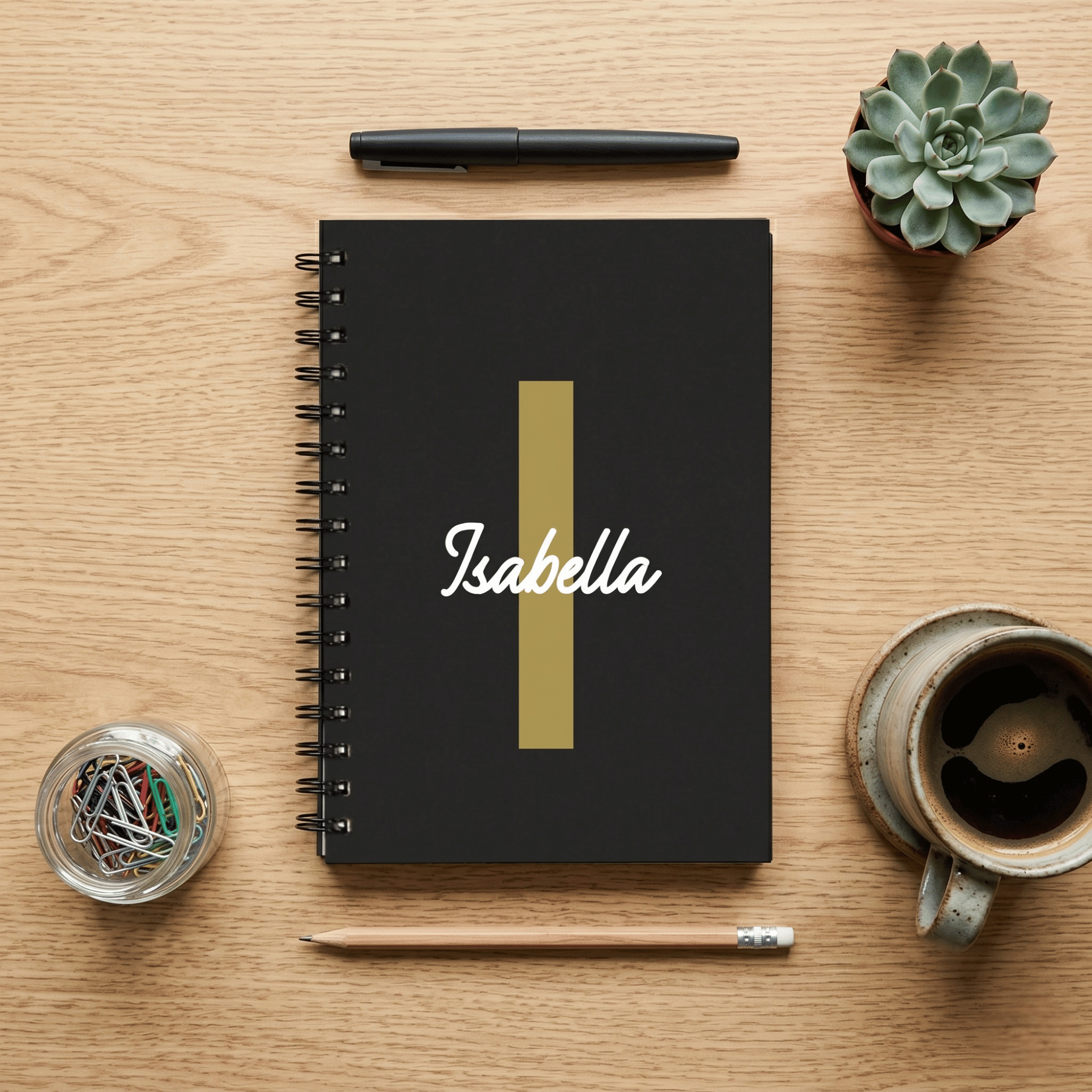 Black notebook with 'Isabella' on a wooden surface with stationery items.