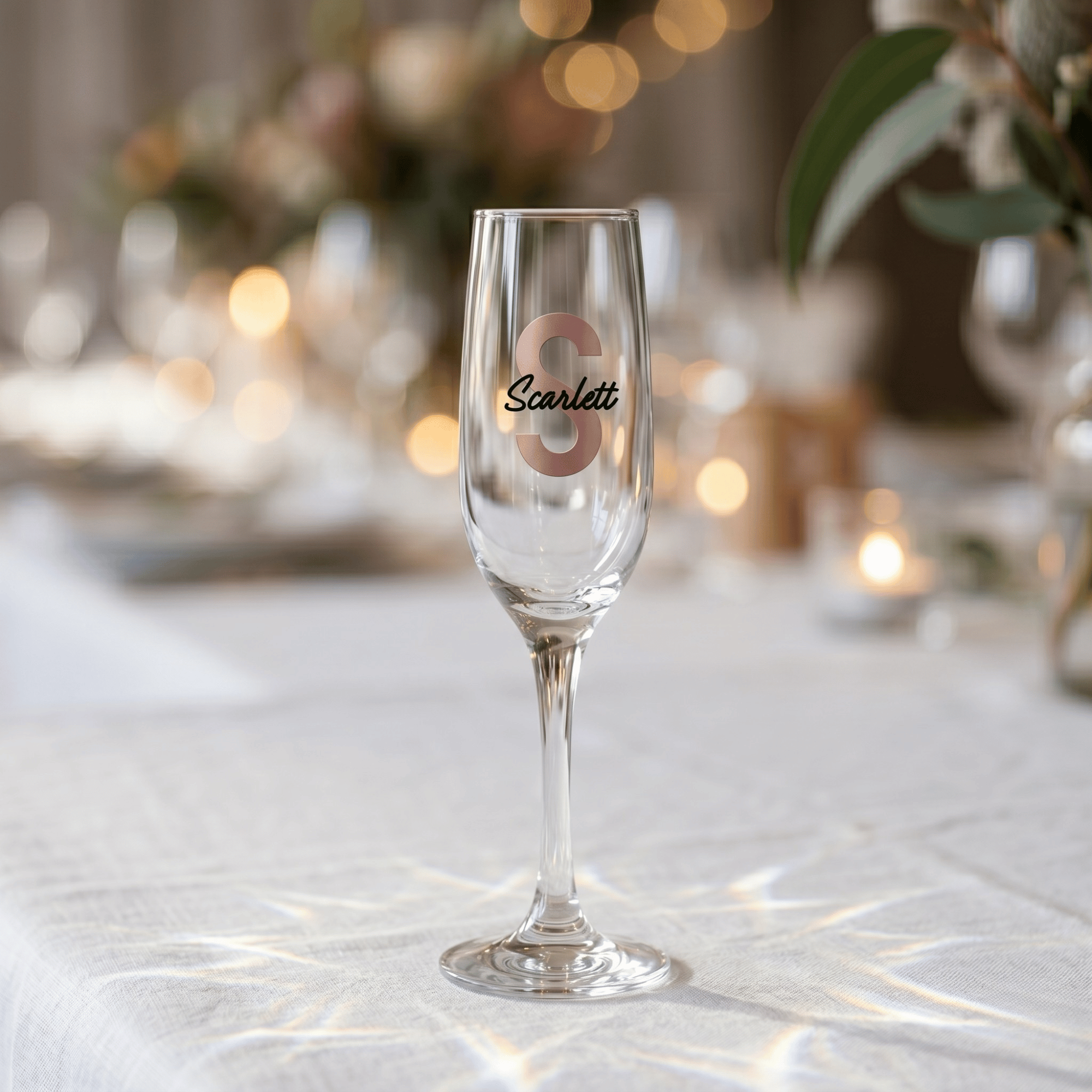Champagne flute with 'Scarlett' engraved on a table with blurred lights and decorations