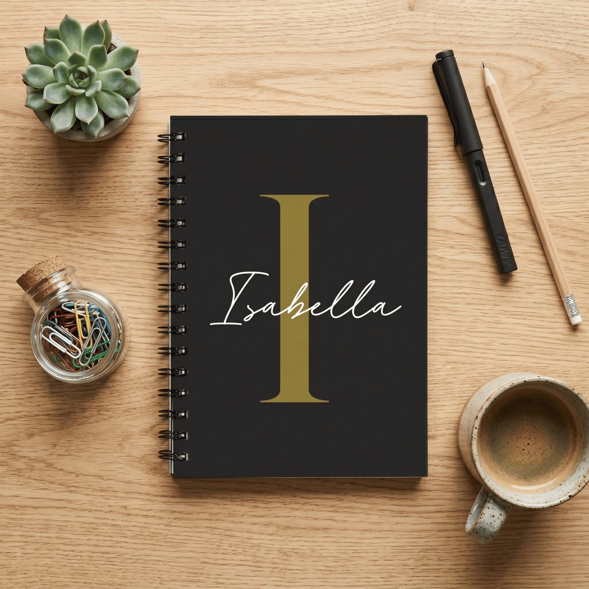 Black notebook with 'Isabella' on a wooden desk with stationery items