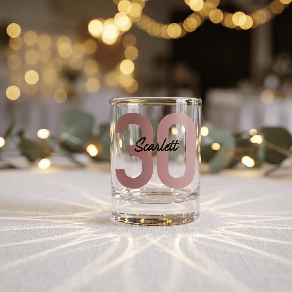 Clear glass with pink number '30' and name 'Scarlett' on a blurred festive background